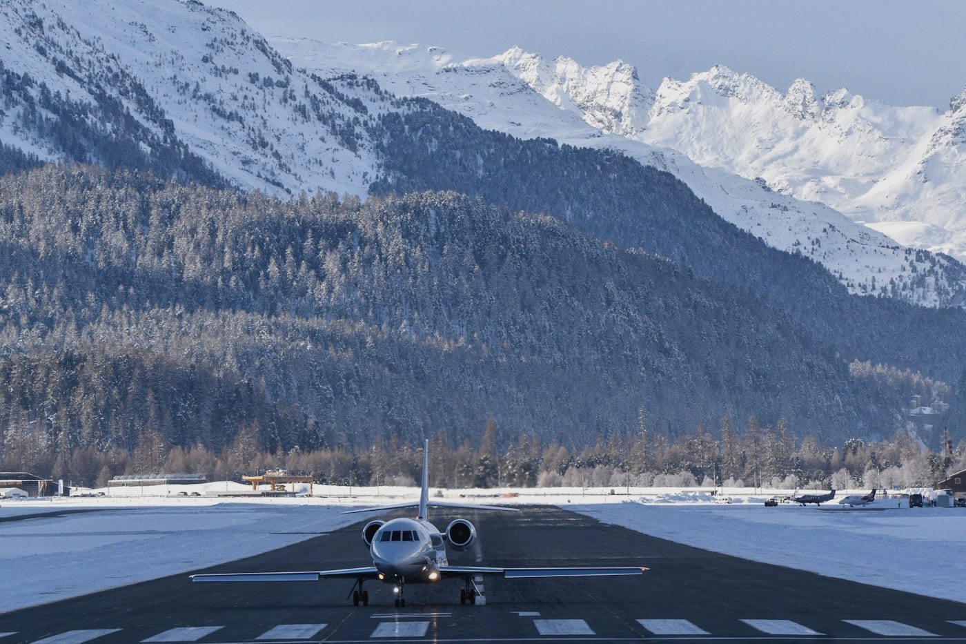 An unmarked white business jet holding on the runway at Samedan, the snow-covered peaks of the Engadin filling the sky behind it.
