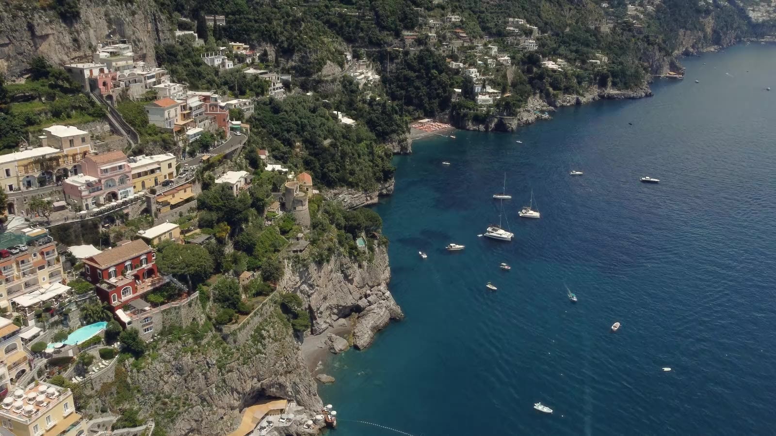 An aerial view of Positano on Italy's Amalfi Coast: pastel houses on the cliffs above the sea, with sailing boats at anchor in the bay.