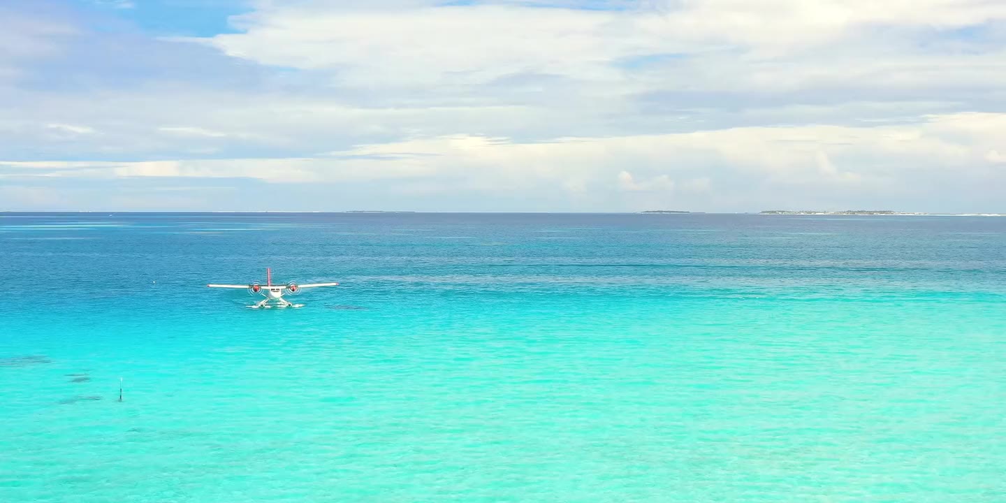 A seaplane at rest on flat turquoise water, low islands on the horizon under a wide sky.